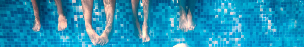 Two adult and two children feet underwater in a pool.